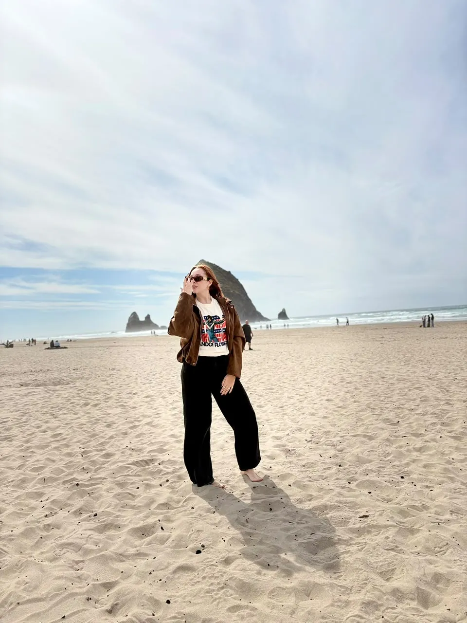 Andreina Aguilar de cuerpo entero, de pie en una playa amplia junto al mar, con una formación rocosa al fondo